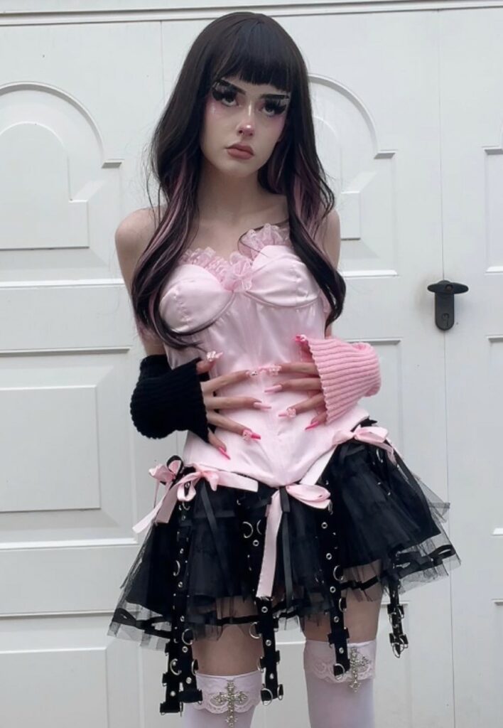 Pastel goth aesthetic outfit idea: satin pink corset top with black & pink hand warmers, mesh mini skirt with garters - by sxcorpionhoe